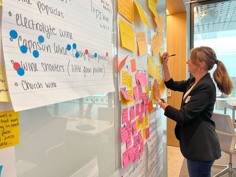 A UC student participates in a design thinking project by placing post-it notes and stickers on a board.